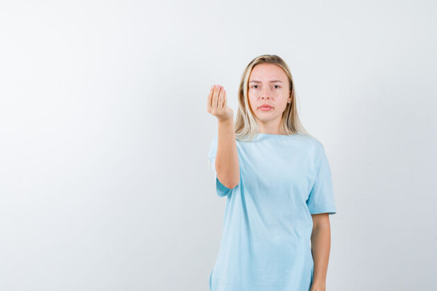 夏天一个金发女孩穿着蓝色t恤展示着意大利的姿态 看起来很严肃 正前方的风景前面肖像手势