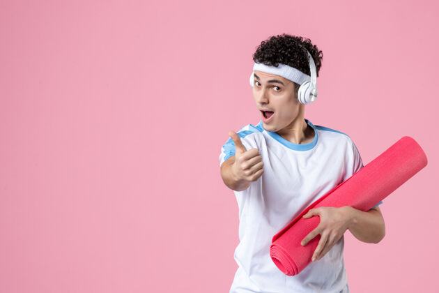 查看正面图穿着运动服的年轻男性 粉色墙上有瑜伽垫锻炼垫子运动