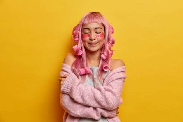 垫迷人迷人的粉色头发女人 温柔地拥抱自己 享受温暖套头衫的柔软 戴着卷发 打造完美的发型黄色乐观染色