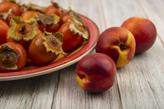 午餐新鲜柔软多汁的柿子放在盘子里 桃子被隔离在灰色的木墙上柔软秋天木头