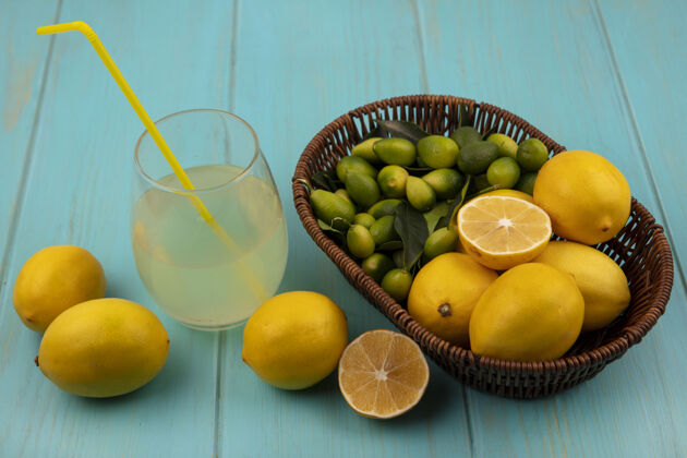 水果新鲜水果的俯视图 如柠檬和金盏花放在一个桶里 新鲜的柠檬汁放在一个玻璃杯里 柠檬被隔离在蓝色的木墙上素食者果汁饮食