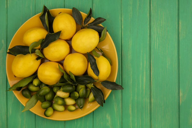 人一个黄色的新鲜柑橘类水果 如柠檬和金盏花在一个绿色的木制墙壁与复制空间顶视图农业水果柑橘