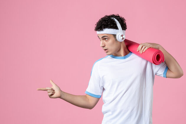 垫子正面图：穿着运动服的年轻男性运动员 粉色墙上有瑜伽垫视图指点个人