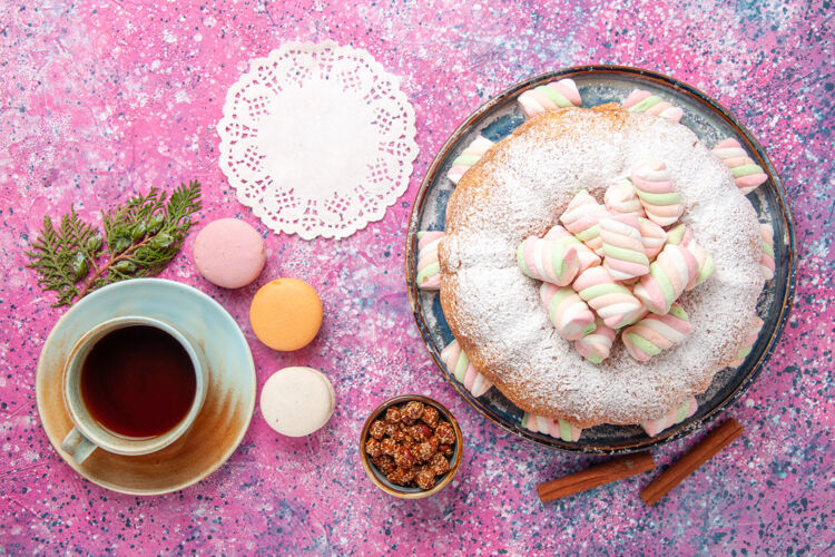 糖粉红色桌子上的糖粉蛋糕和一杯茶和法国马卡龙的俯视图生的麦卡龙茶