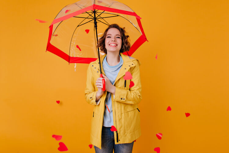 优雅幸福的苍白女孩穿着时髦的夹克站在阳伞下真诚的微笑年轻女子穿着优雅的秋装摆在黄色的墙上雨明亮年轻