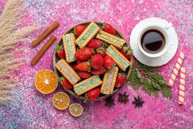 顶视图俯瞰美味的华夫饼干 新鲜的红色草莓和粉红色表面上的一杯茶美味华夫饼茶