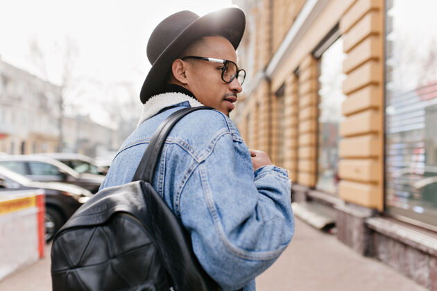 时尚户外照片来自自信的非洲男子穿着牛仔夹克走在街上时尚的黑人男子在看展示年轻休闲周末