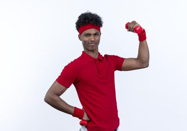 男人紧张的年轻美国黑人运动男子戴着头带和手腕举起哑铃隔离在白色年轻表情腕带