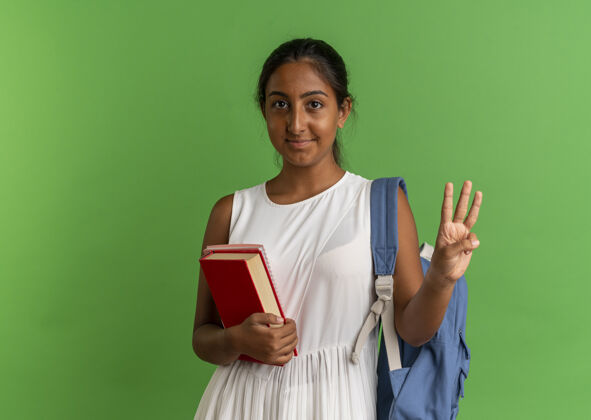 背高兴的小女生背着书包拿着带笔记本的书 手上拿着三个绿色的手笔记本年轻的