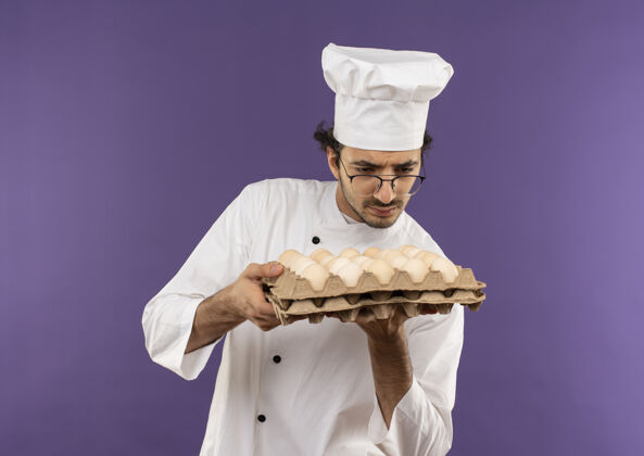 厨师想着年轻的男厨师穿着厨师制服 戴着眼镜 拿着紫色的鸡蛋看着一批批批年轻眼镜