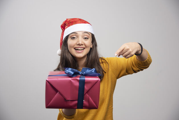 冬天戴着圣诞帽的微笑女人展示着一个礼品盒漂亮女士微笑