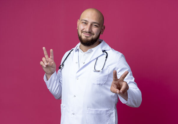 听诊器高兴的年轻男医生穿着医用长袍和听诊器显示出良好的手势隔离粉红色手势医疗年轻