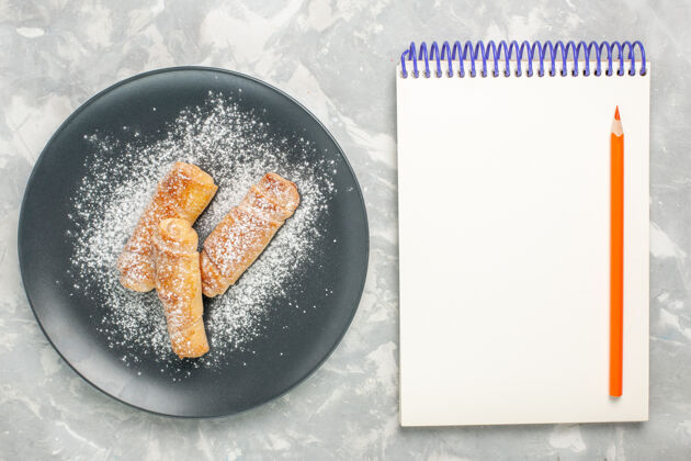 炊具白色表面上带有记事本的糖粉百吉饼俯视图含糖美味烹饪