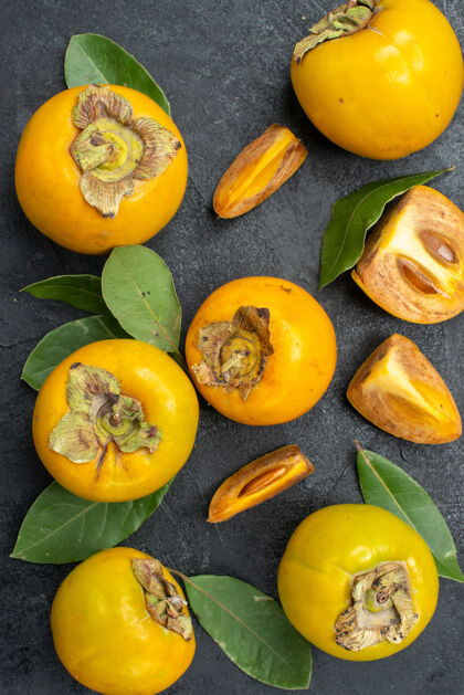 黄顶视图新鲜甜甜的柿子和叶子放在深色的桌子上品尝水果食味秋