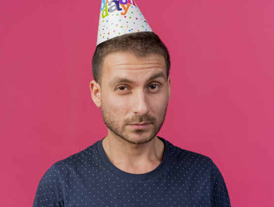 脸自信的帅哥戴着生日帽望着前面孤立的粉色墙壁表情姿势衣服