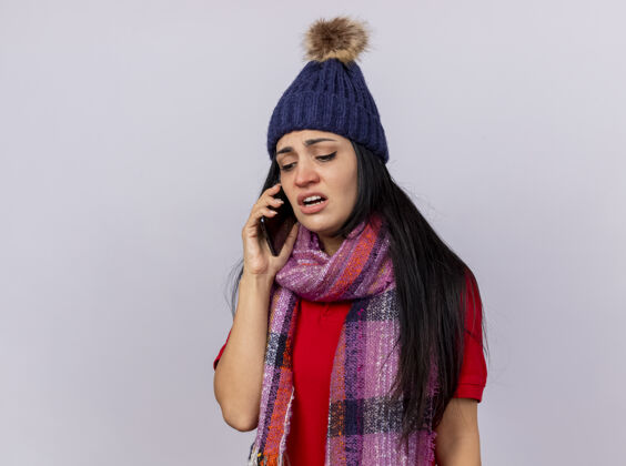 脸愁眉不展的年轻病女人戴着冬天的帽子和围巾在打电话 孤零零地看着白墙穿着人冬天