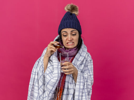添加一个戴着冬日帽 围着方格布围巾 往隔离在粉红色墙上的一杯水里加药的年轻病妇表情冬天格子