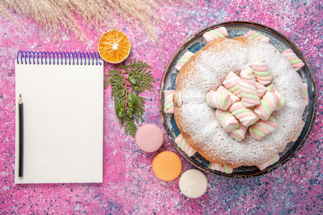食物糖粉蛋糕的俯视图 粉色表面有甜棉花糖和记事本顶视图烘焙糖