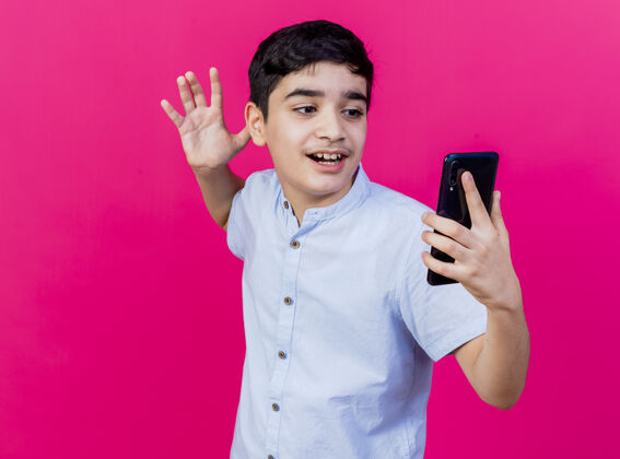 手机印象深刻的小男孩手里拿着手机 看着手机 手在空气中隔离在粉红色的墙上市民保持握着