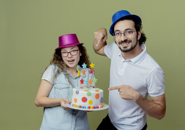 绿色微笑着的年轻夫妇戴着粉色和蓝色的帽子 男人指着她手上橄榄绿的生日蛋糕微笑蛋糕生日