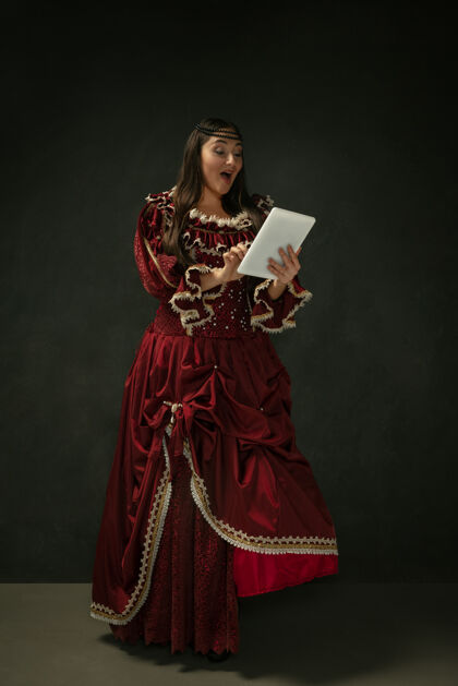 命运中世纪年轻女子的肖像在红色复古服装上使用黑色背景的平板电脑历史砖城堡