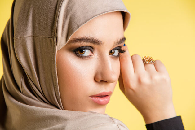 情绪美丽的年轻阿拉伯妇女在时尚的头巾隔离在黄色背景与空间姿势围巾微笑