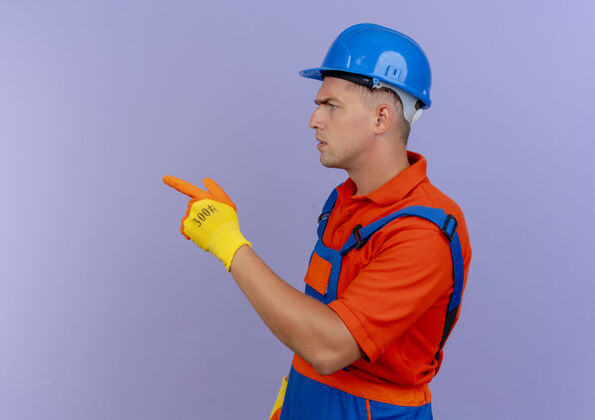 手套站在剖面图上的年轻男性建设者身穿制服 戴着安全帽 手套指向紫色的侧面男性头盔安全