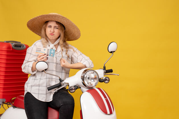 举行雄心勃勃的年轻女子戴着帽子 坐在摩托车上 拿着车票 听着黄色的最后一句闲话帽子摩托车最后