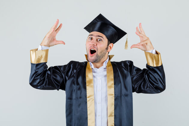 毕业身着毕业制服的年轻人举手 惊讶地看着前方自信成功男人