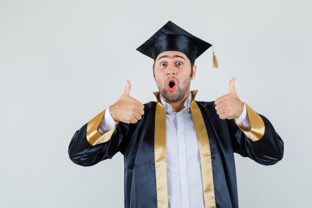 年轻身穿毕业制服的年轻人竖起大拇指 看上去很幸福 正面照休闲站立毕业