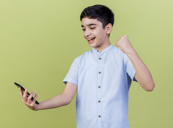 人快乐的小男孩抱着手机看着橄榄绿的墙上做着“是”的手势市民姿势抱着