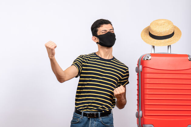 红色正面图是一个戴着黑色面具的年轻游客 站在红色的手提箱旁展示他的拳头肖像男人近