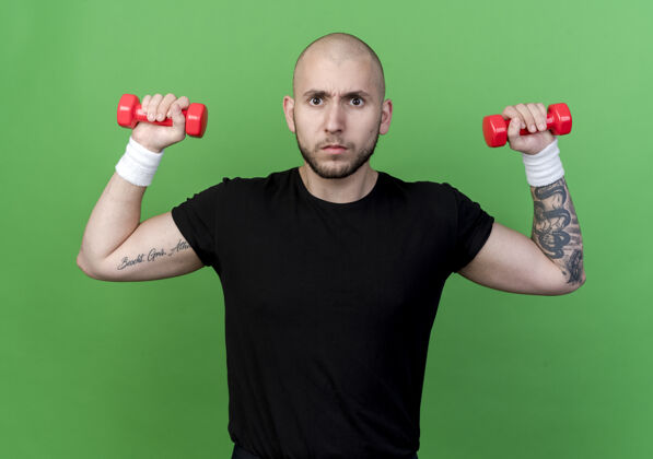 年轻严格的年轻运动男子戴着腕带锻炼哑铃隔离在绿色哑铃腕带男人