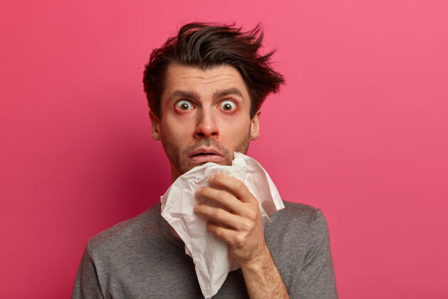 不健康晕眩的病人有流感 病毒或呼吸道过敏 眼睛发红 用组织擤鼻涕 发现严重疾病 在粉红色的墙壁上摆姿势健康 药物和症状概念男人组织白种人