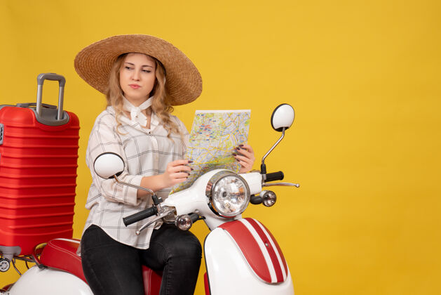 肖像惊讶的年轻女子戴着帽子 坐在摩托车上 手里拿着黄色的地图帽子年轻女子成人
