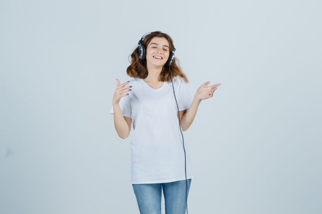 耳机年轻女性穿着白色t恤 牛仔裤 戴着耳机欣赏音乐 看起来很开心 正面照惊喜面部卷发