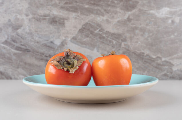营养放在大理石上的蓝色盘子上的东方柿子健康配料风味