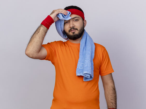 湿巾疲惫的年轻运动男子戴着头带和腕带擦额头用毛巾隔离在白色背景上疲倦运动前额