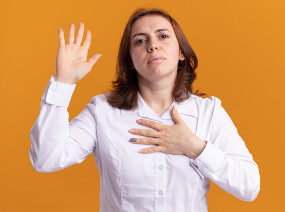 制造身穿白衬衫的年轻女子站在橘色的墙上 严肃地抬起脸看着前面 许下诺言手衬衫提高