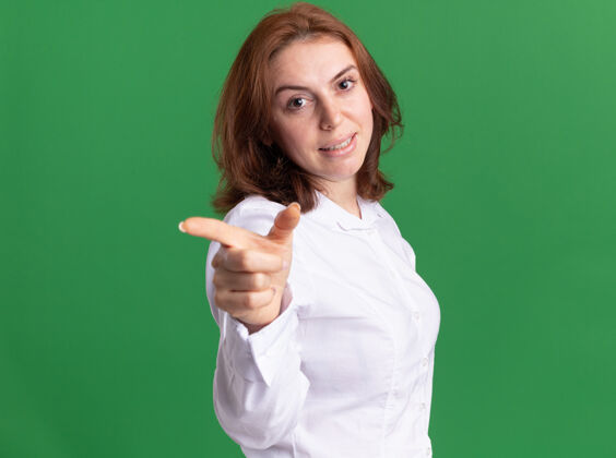 女人身穿白衬衫的年轻女子站在绿色的墙壁上 微笑着用食指指着前面指着目录站着