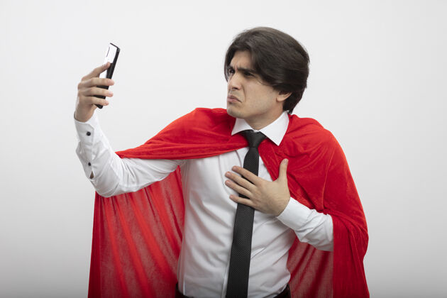 领带一个年轻的超级英雄戴着领带 手放在胸前看着手机 被隔离在白色背景下手年轻人电话