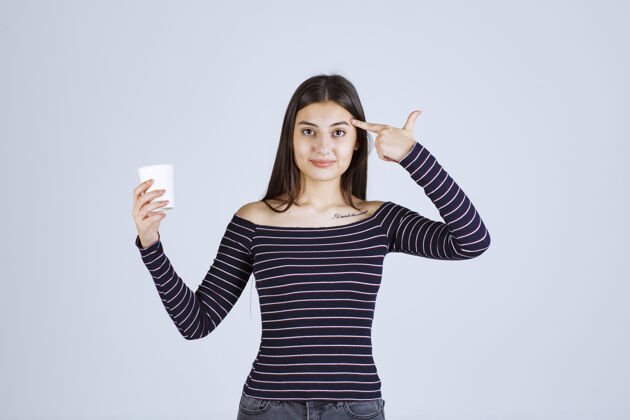 年轻人穿着条纹衬衫的女孩拿着一个塑料咖啡杯在思考姿势休闲年轻