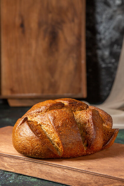 面包整个黑面包的垂直视图在深色表面上的棕色木砧板上新鲜整个颜色
