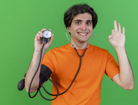 好的微笑的年轻病人戴着听诊器 手持血压计 在绿色背景上显示出良好的姿势年轻微笑疾病