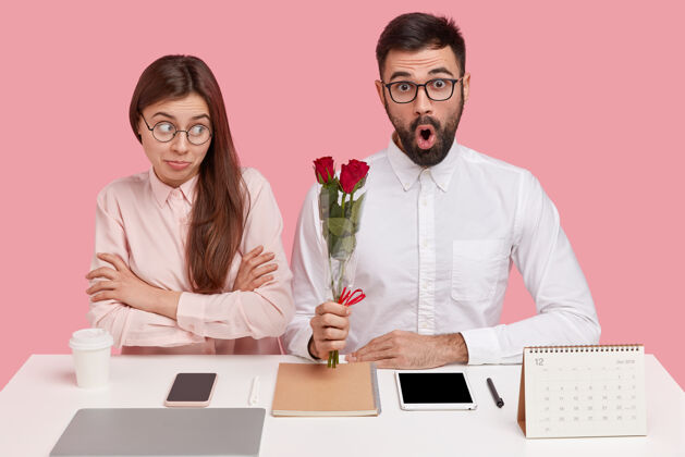 惊喜坐在书桌旁的年轻夫妇和捧着玫瑰花束的男人女性电话花束