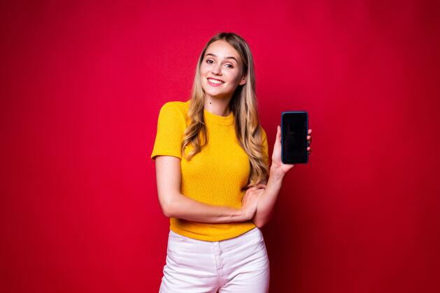 墙幸福的女人微笑着 在红墙外隔离的手机黑屏上指指点点屏幕女孩互联网