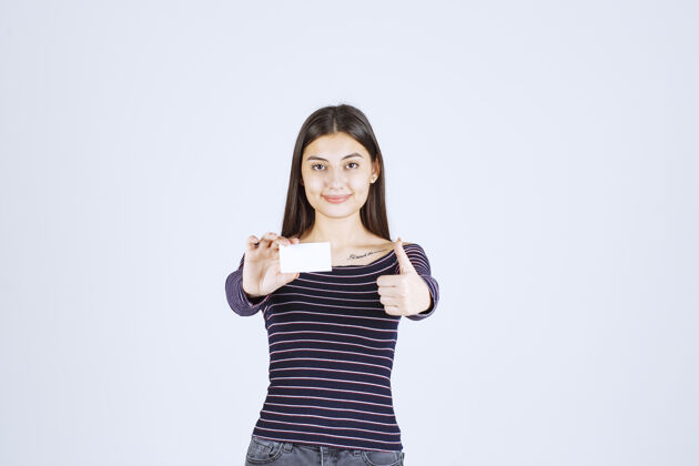 成功穿条纹衬衫的女孩拿着名片 举着拇指朝上的牌子伙伴关系年轻年轻人