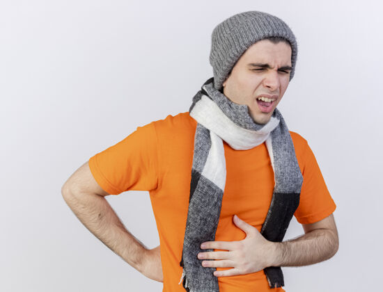 胃闭着眼睛 戴着冬天的帽子 戴着围巾 手放在疼痛的肚子上 隔离在白色的背景上 一个未被释放的年轻病人围巾疾病疼痛