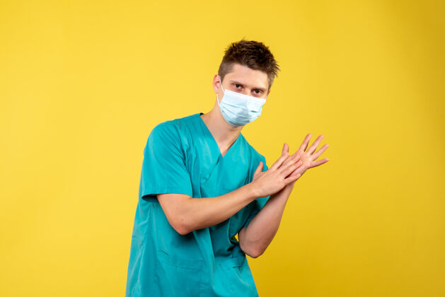 男性黄墙上的男医生穿着医疗服 戴着无菌口罩成人人面具