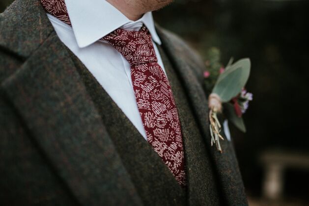 新人特写镜头新郎的西装与鲜花和红色图案领带与树木的背景浪漫婚礼丈夫